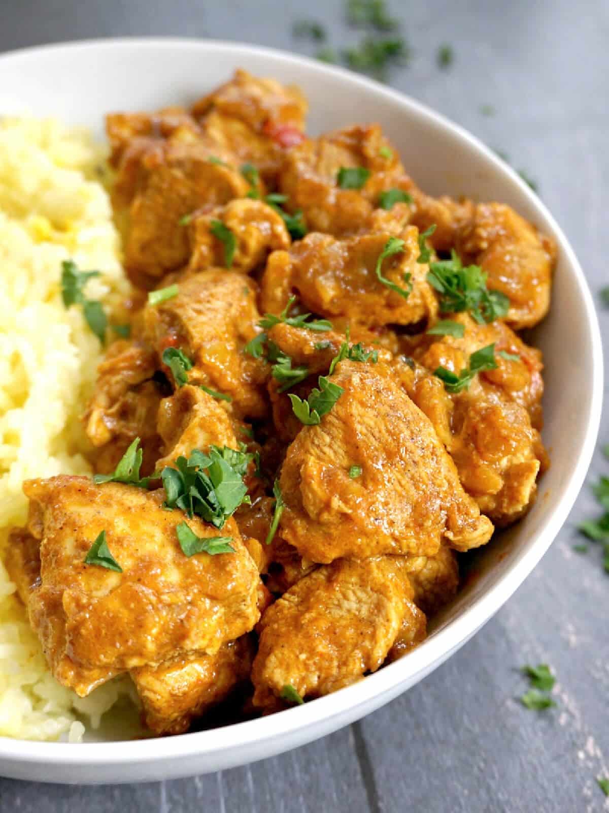 A white bowl with chicken balti and rice.