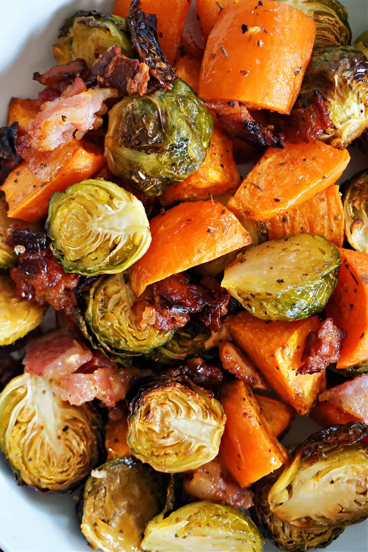 A portion of roasted brussel sprout halves, sweet potatoes and bacon.