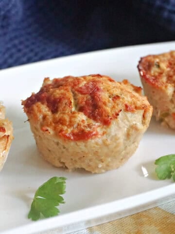 A white rectangle plate with 3 meatloaf muffins and parsley leaves around.