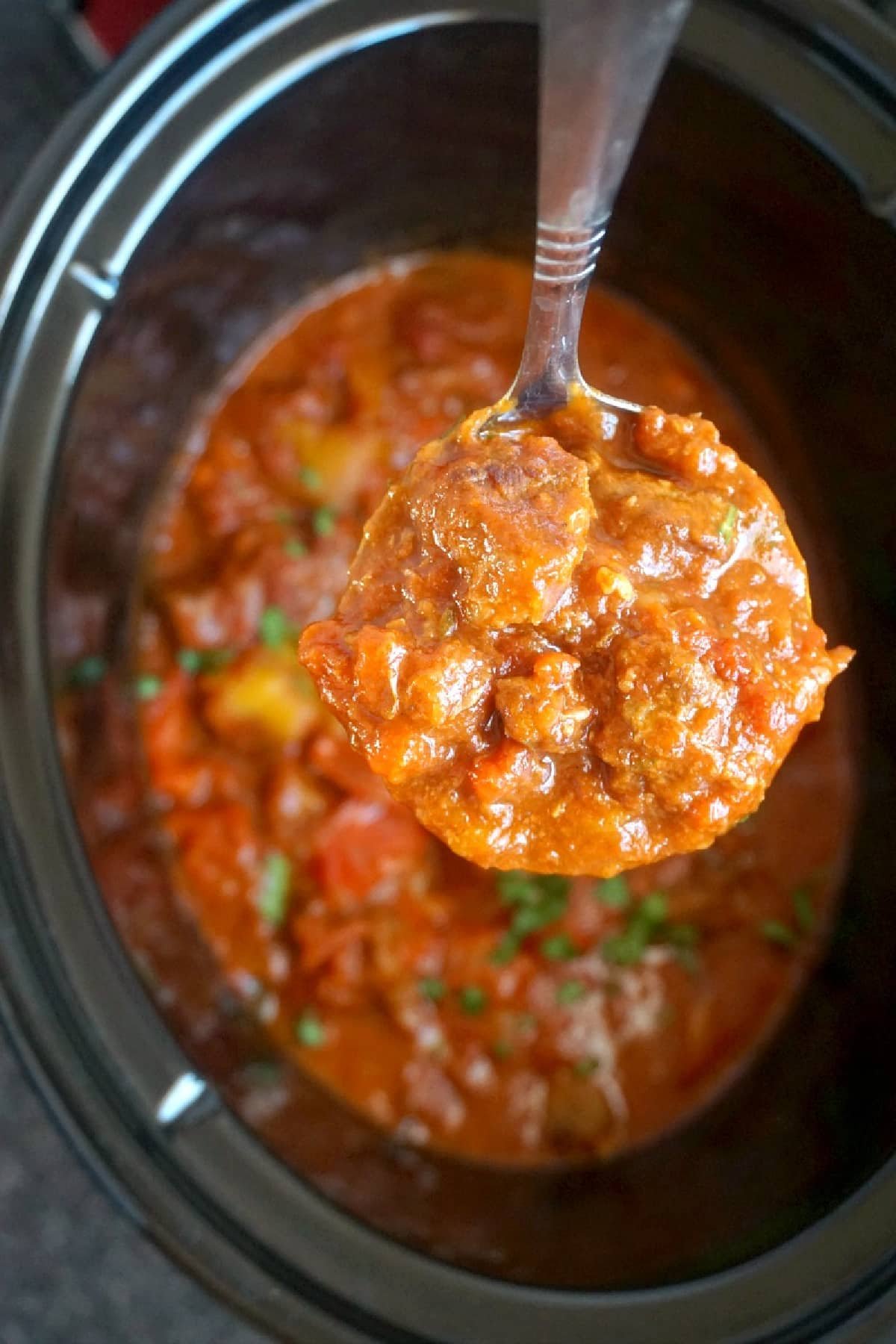 A ladleful of goulash on top of a crockpot.