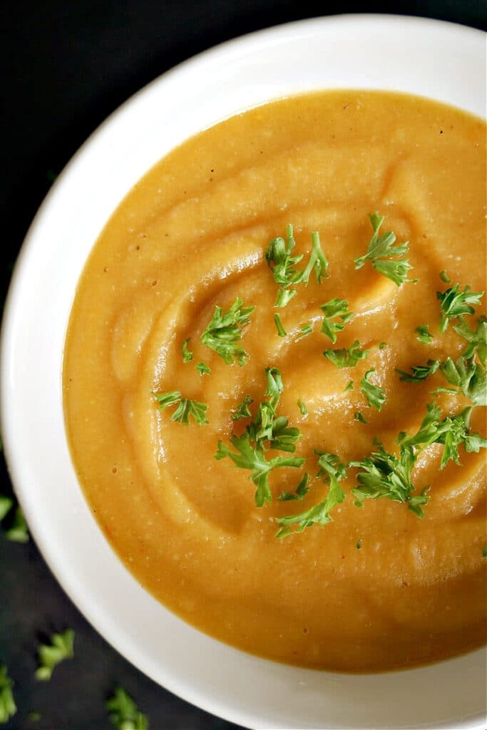 Overhead shoot of a white bowl with creamed sweet potato soup garnished with parsley