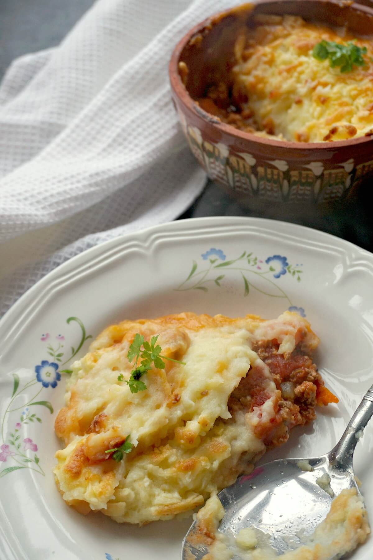 A white plate with turkey cottage pie and a pot with more pie in the background.