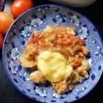 A blue plate with a portion of crumble topped with custard.