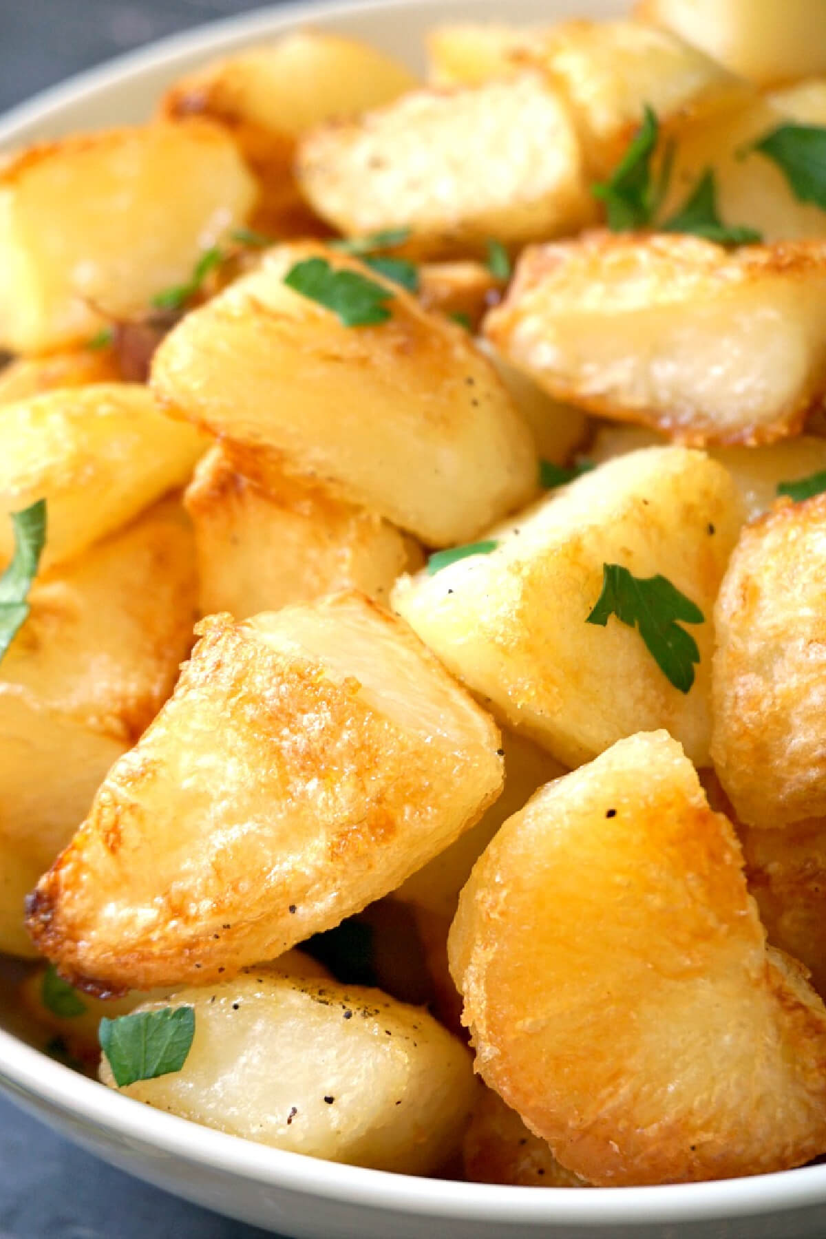 Close-up shoot of roast potatoes in a white bowl.