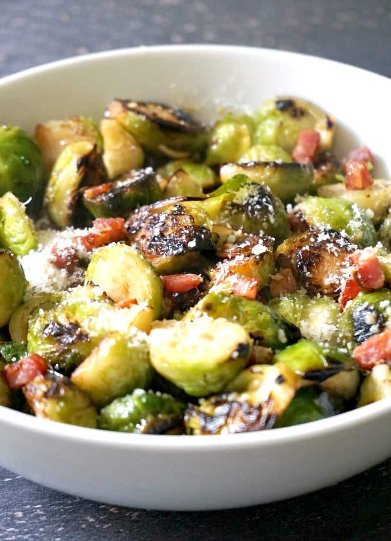 A white bowl with sauteed brussels sprouts, bacon and parmesan.
