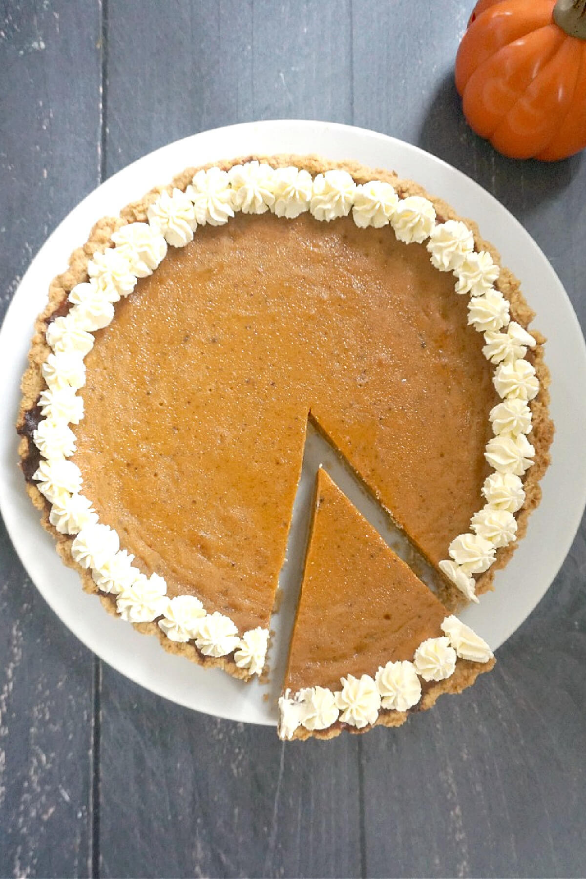 Overhead shoot of a white plate with a pumpkin pie and a slice cut out of it