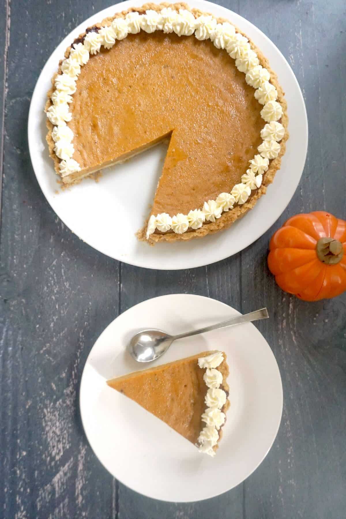 Overhead shoot of a white plate with a slice of pumpkin pie and another plate with the rest of the pie