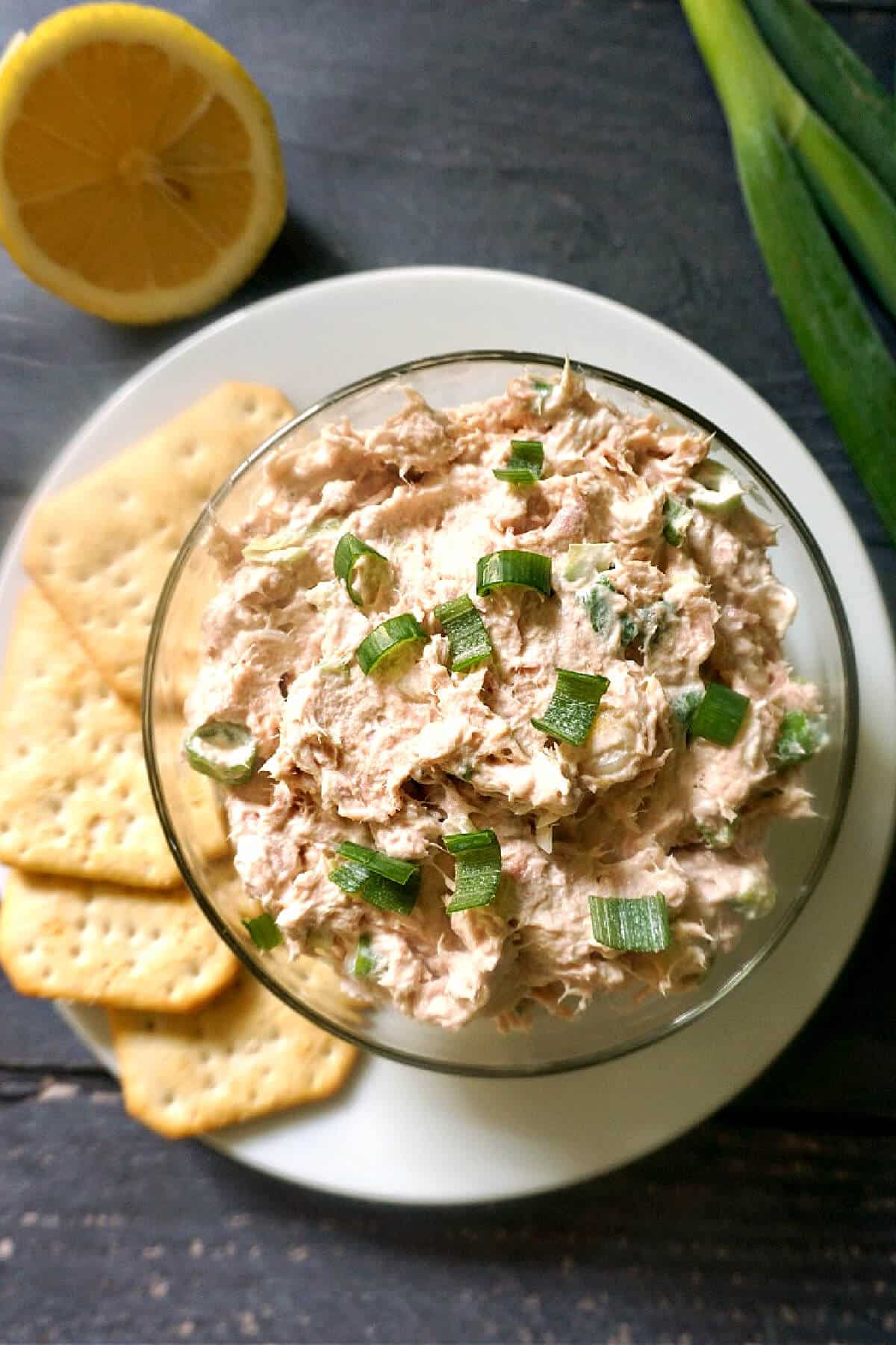 A glass bowl with tuna dip and crackers on the side.