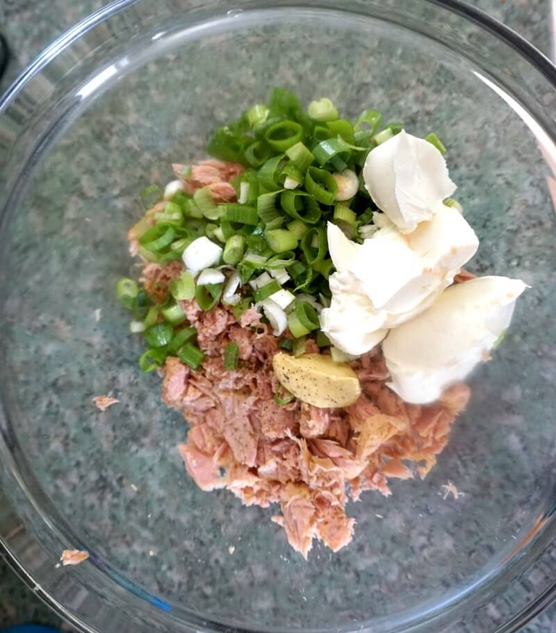 Overhead shoot of a glass bowl with flaked tuna, cream cheese and chopped onions to make a tuna dip