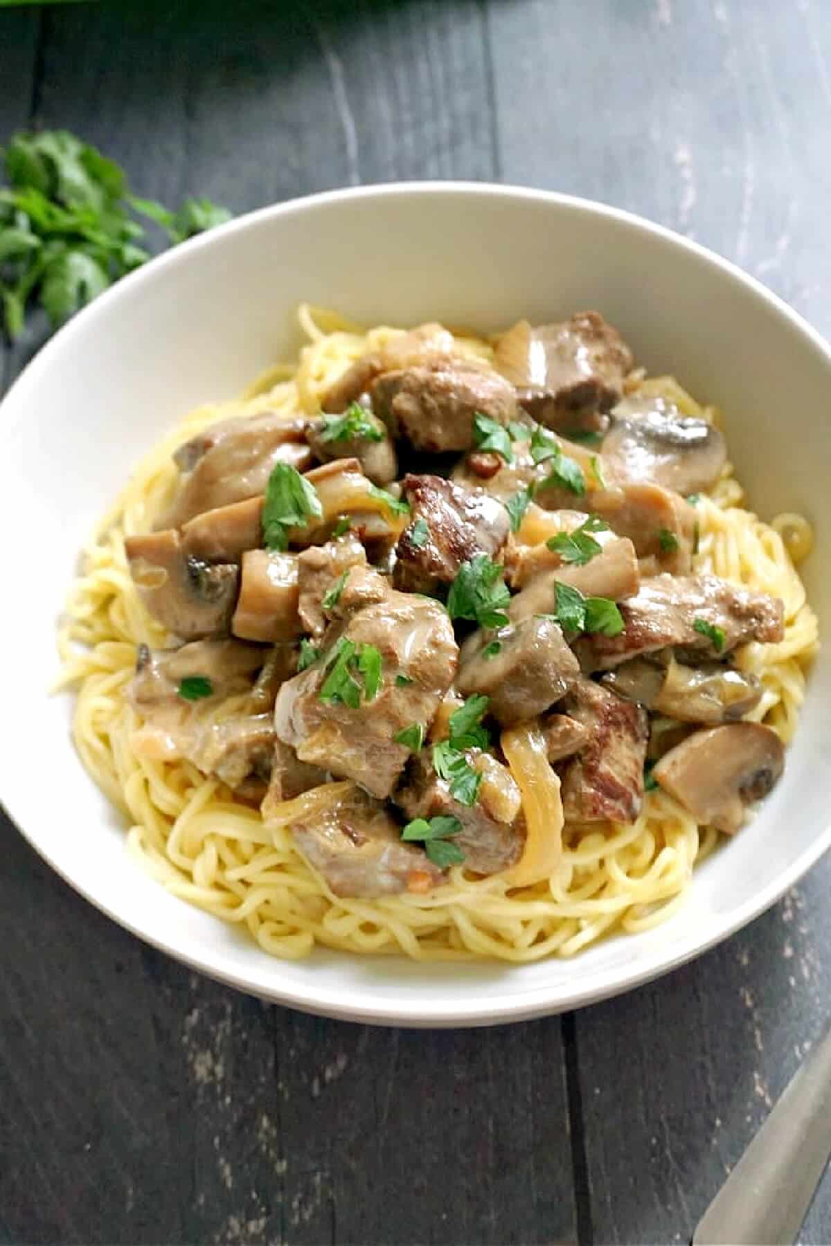 A white bowl with noodles and beef pieces.