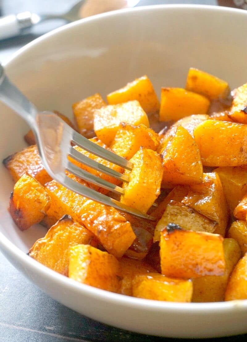 A white bowl with roasted butternut squash with maple syrup and cinnamon and a fork