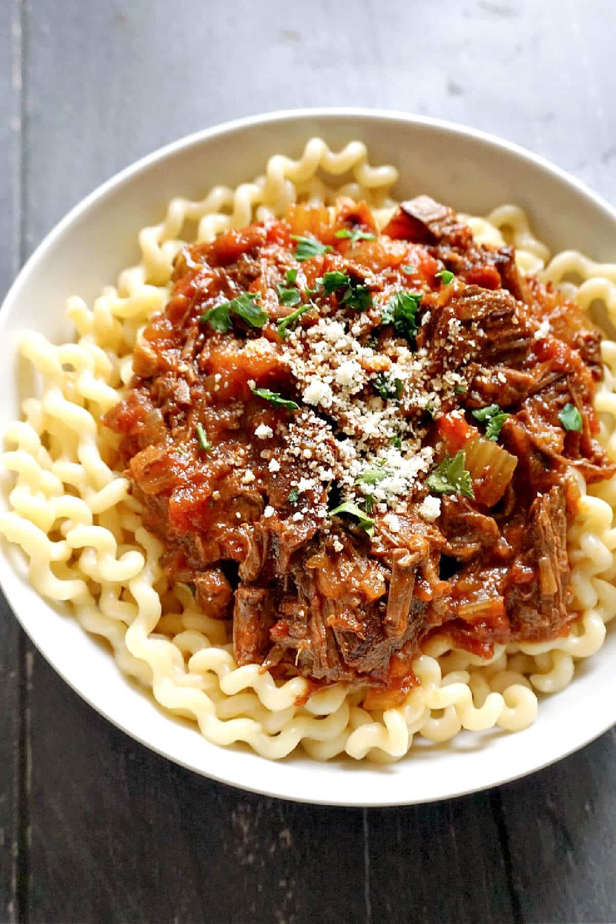 A white plate with pasta and beef ragu on top.