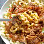 A white bowl with pasta topped with beef ragu