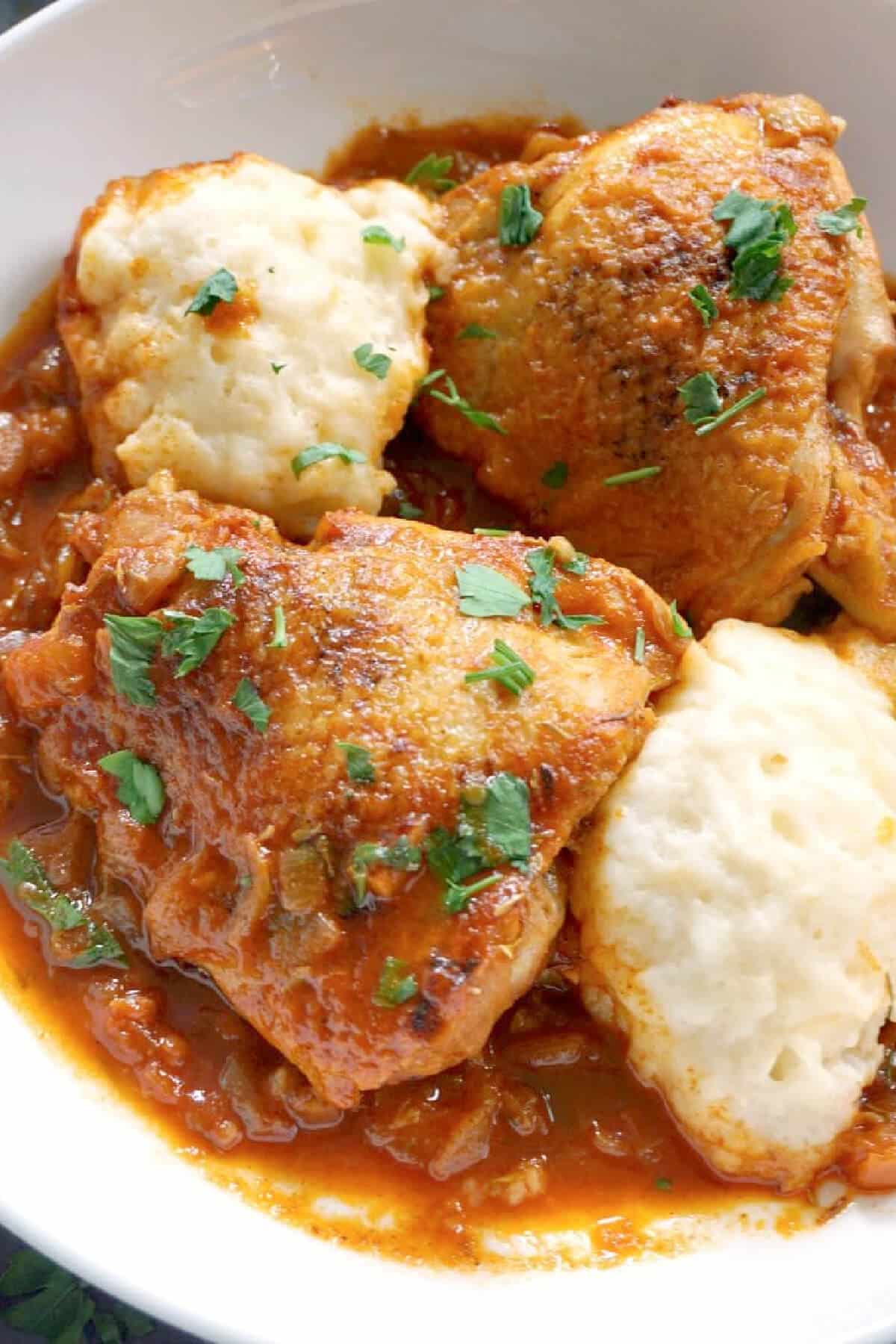 Close-up shoot of a plate with chicken pieces and dumplings.