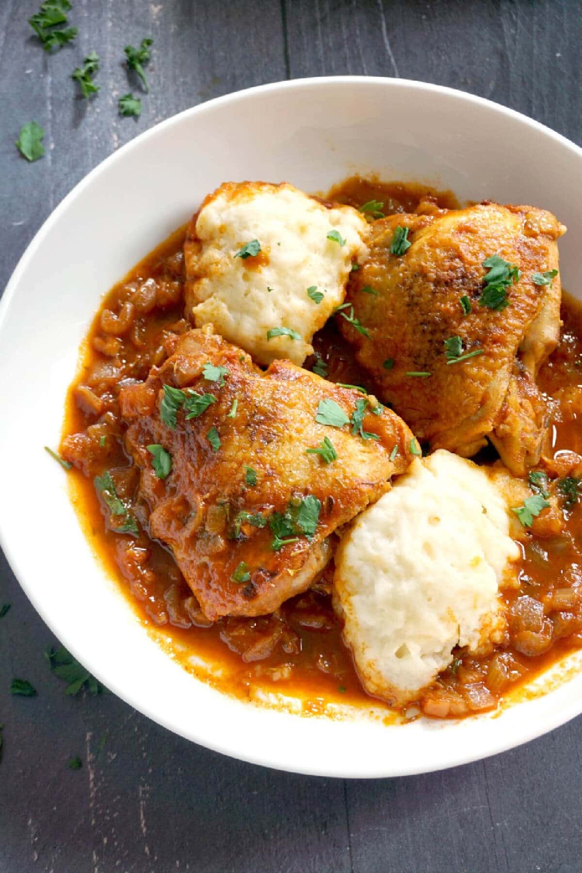 A white bowl with chicken paprikash with dumplings.