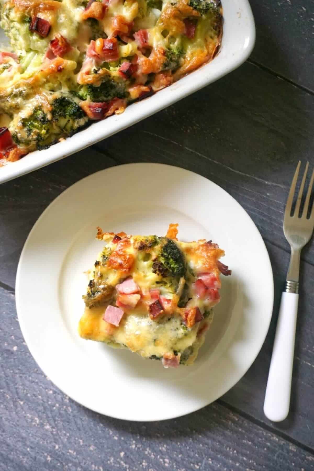 A white plate with a portion of ham and broccoli bake.