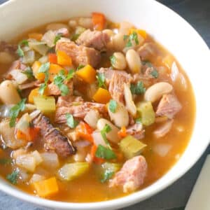 A white bowl with ham and bean soup garnished with fresh parsley