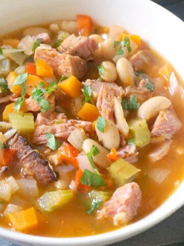 A white bowl with ham and bean soup garnished with fresh parsley