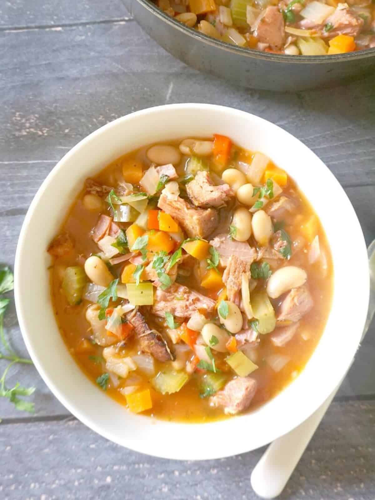 Overhead shoot of a white bowl with ham and bean soup.