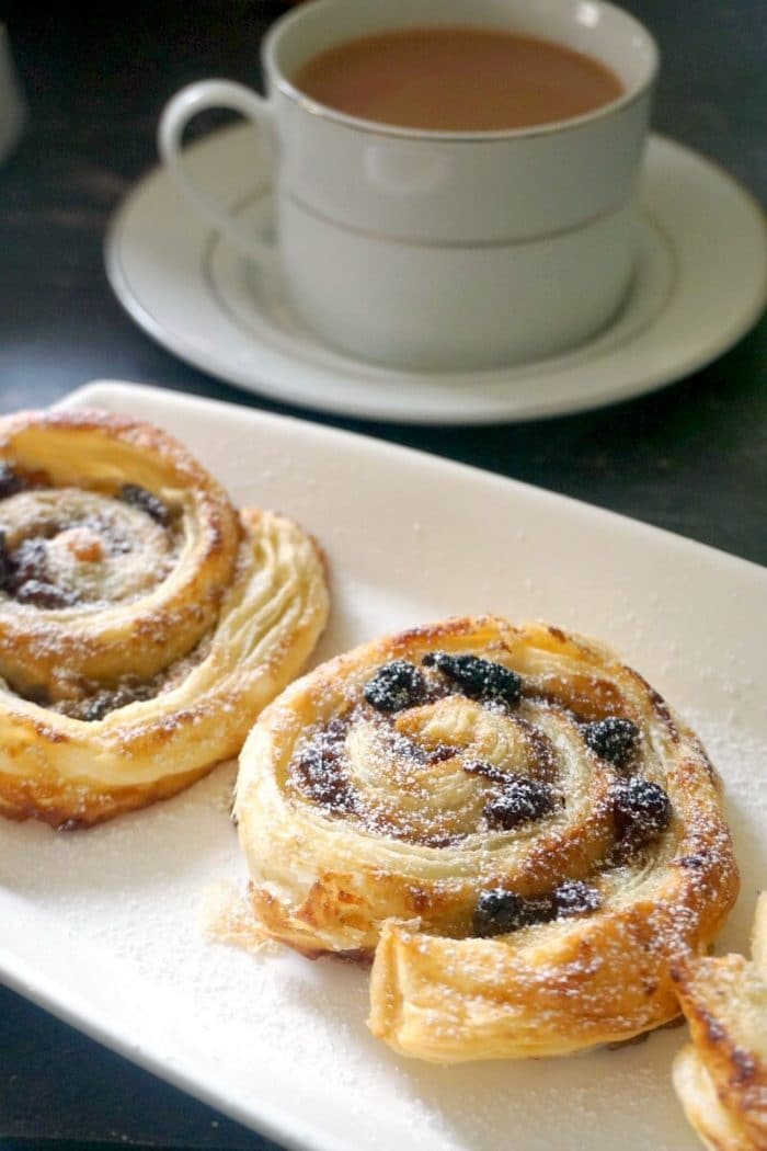 2 mince pie pinwheels on a white rectangle plate with a cup of tea next to it.