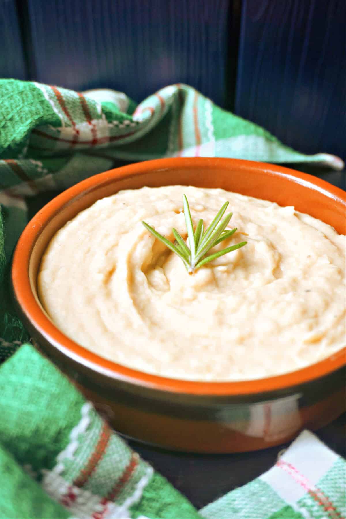 A brown bowl with bean mash garnished with a small rosemary sprig.