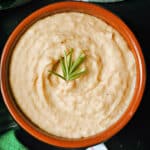 A brown bowl with mash and a spring of rosemary