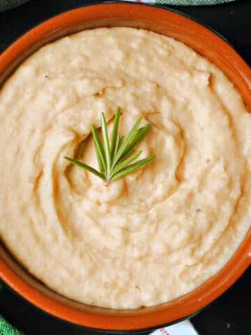 A brown bowl with mash and a spring of rosemary