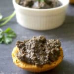 A slice of bread spread with tapenade and a white ramekin with more tapenade