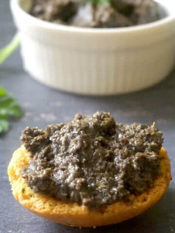 A slice of bread spread with tapenade and a white ramekin with more tapenade