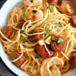 A white bowl of pasta with chorizo and prawns garnished with parsley.