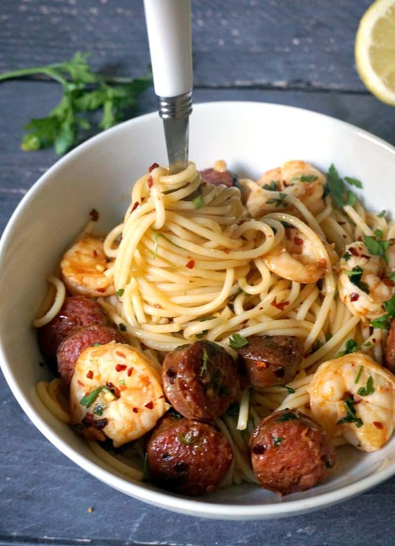 A white bowl of spaghetti topped with chorizo slices and prawns