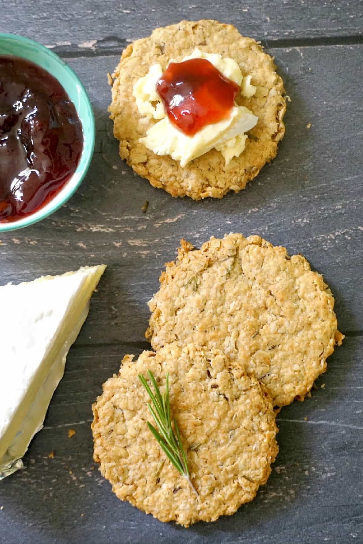 Overhead shoot of 2 oat biscuits with a small bowl of jam, brie cheese and a biscuit top with jam and cheese