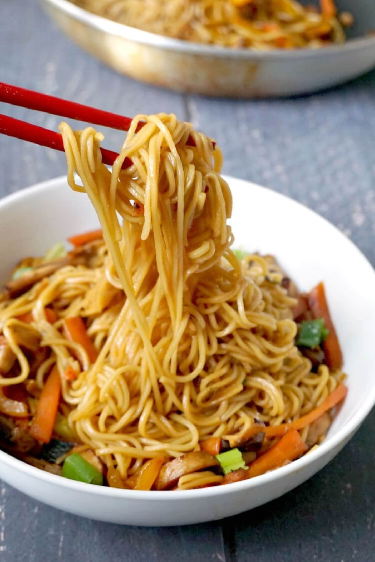 Chopsticks with egg noodles from a white bowl.