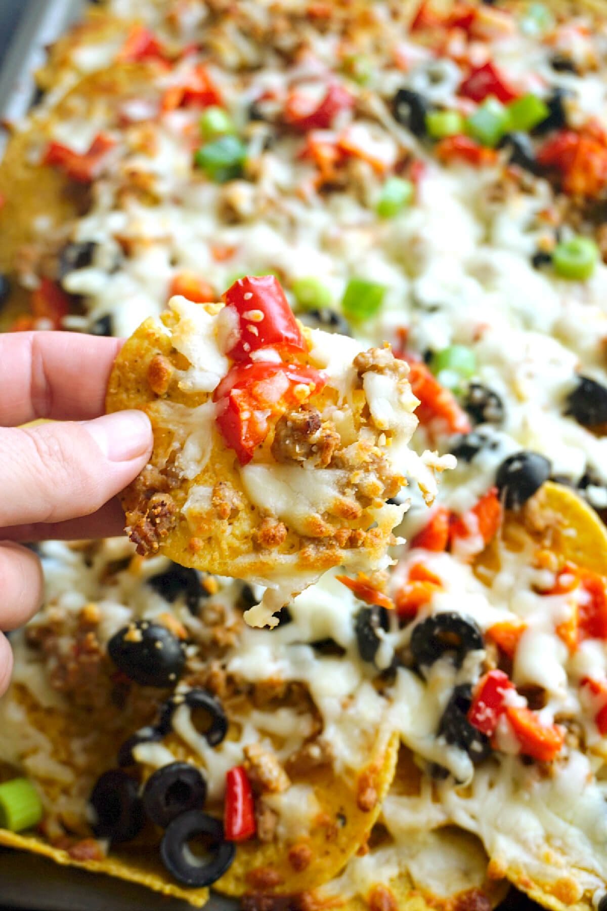 Close-up shoot of nachos loaded with ground pork, cheese and veggies.