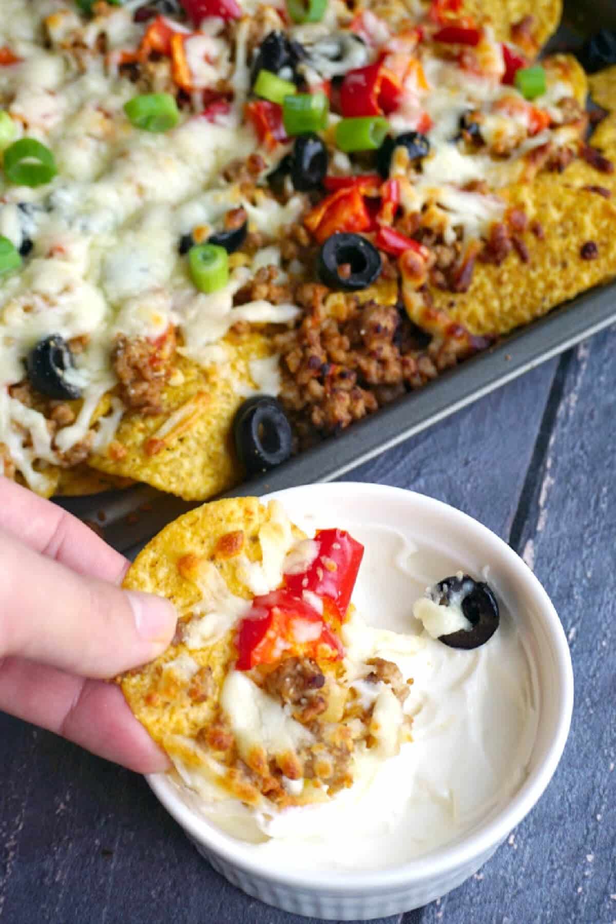 Nachos being dipped into sour cream with a tray of more nachos.