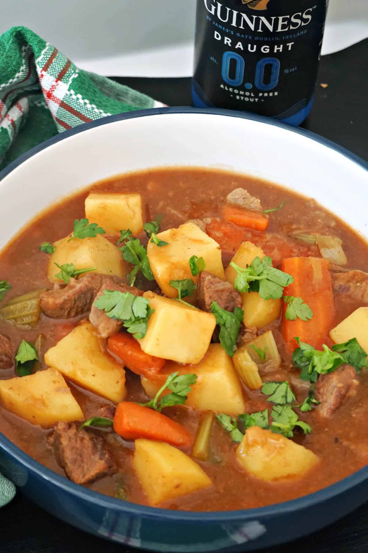 A bowl of beef stew with a can of Guinness in the background.