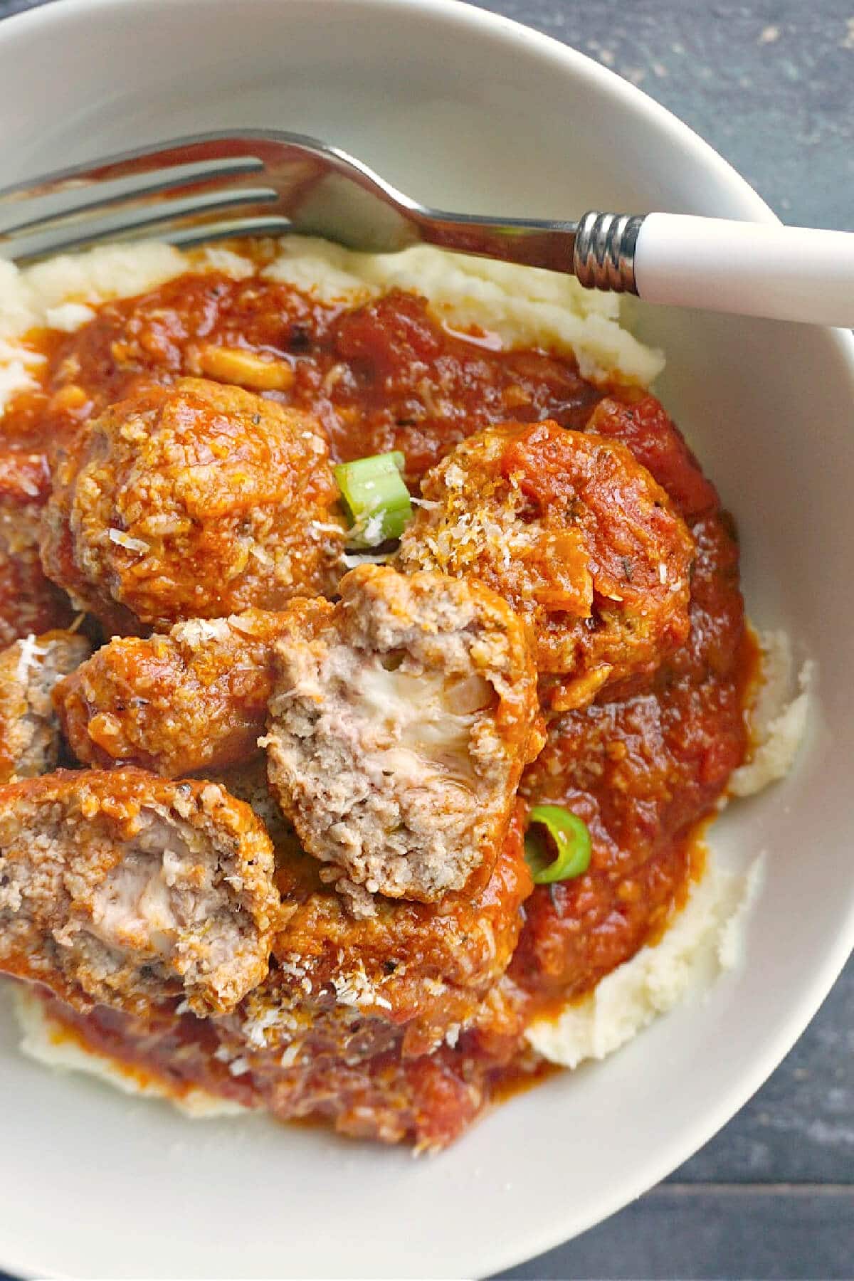 A white plate with meatballs in sauce over a bed of mash.
