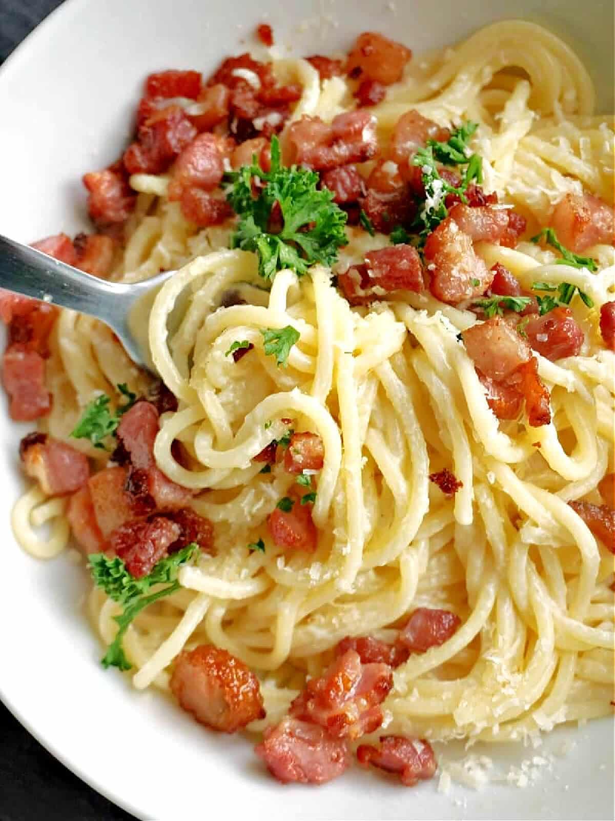 Close-up shoot of spaghetti tossed with bacon lardons and chopped fresh parsley