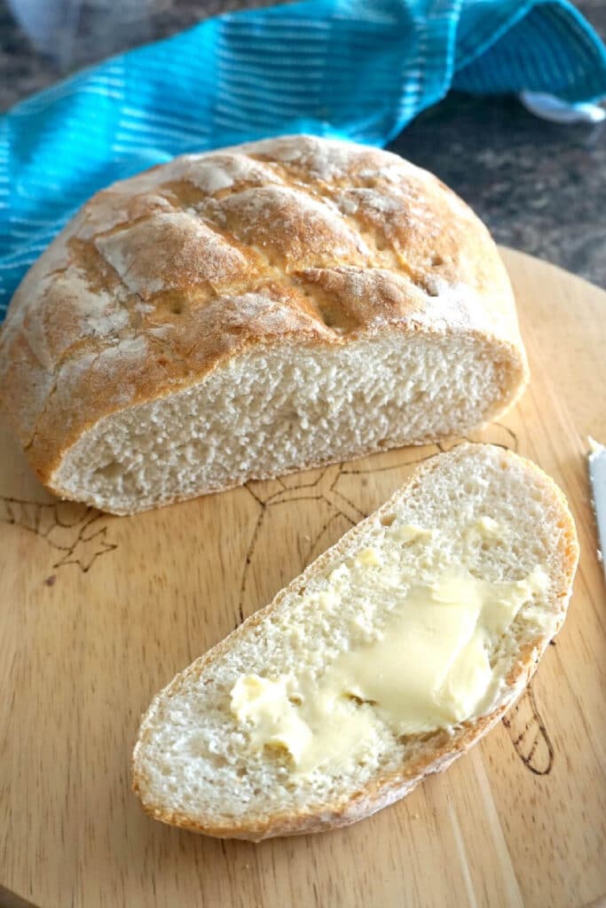 A slice of buttered bread with the rest of the bread on a wooden board