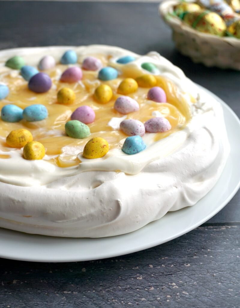 A pavlova topped with cream, lemon curd and chocolate eggs