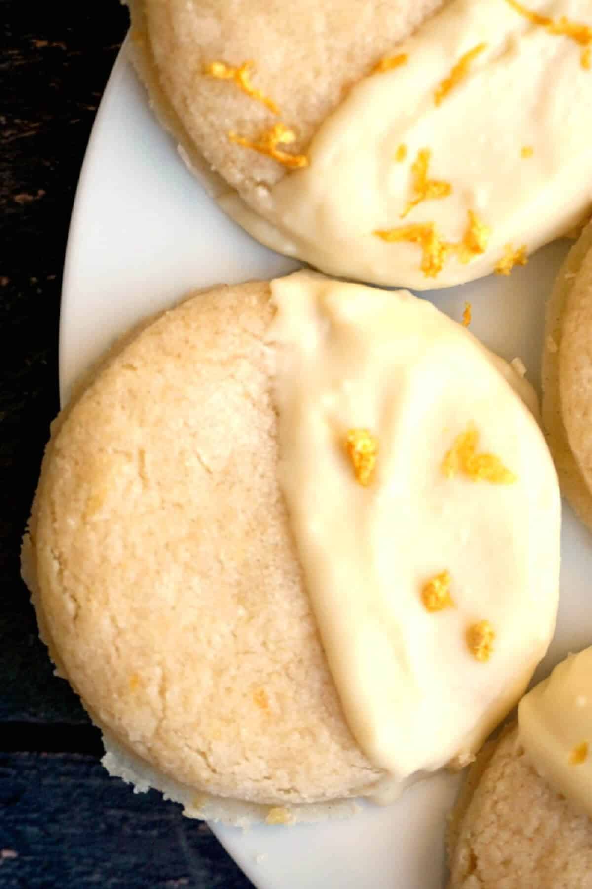 Close up shoot of a cookie half dipped into white chocolate and garnished with lemon zest.