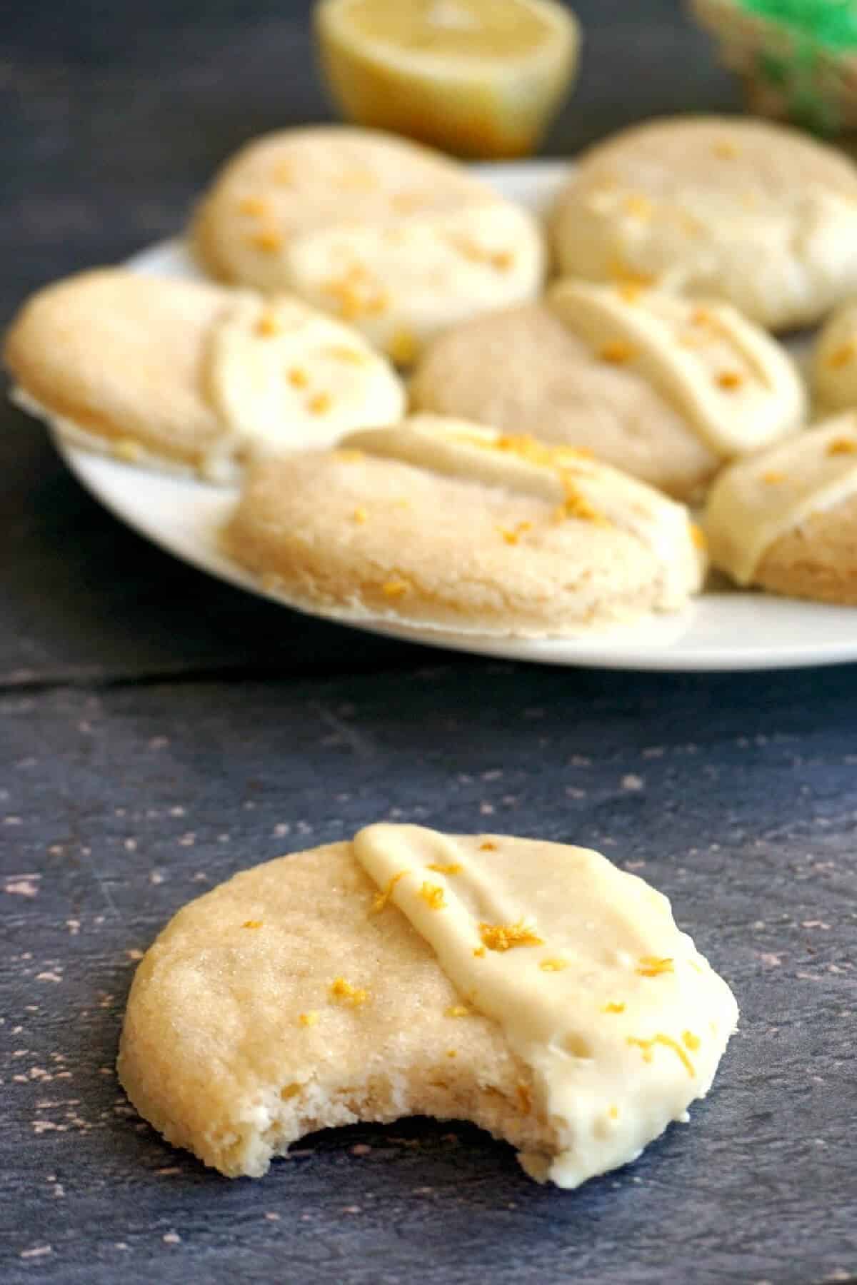 Half a cookie on a table with more cookies on a plate at the top.