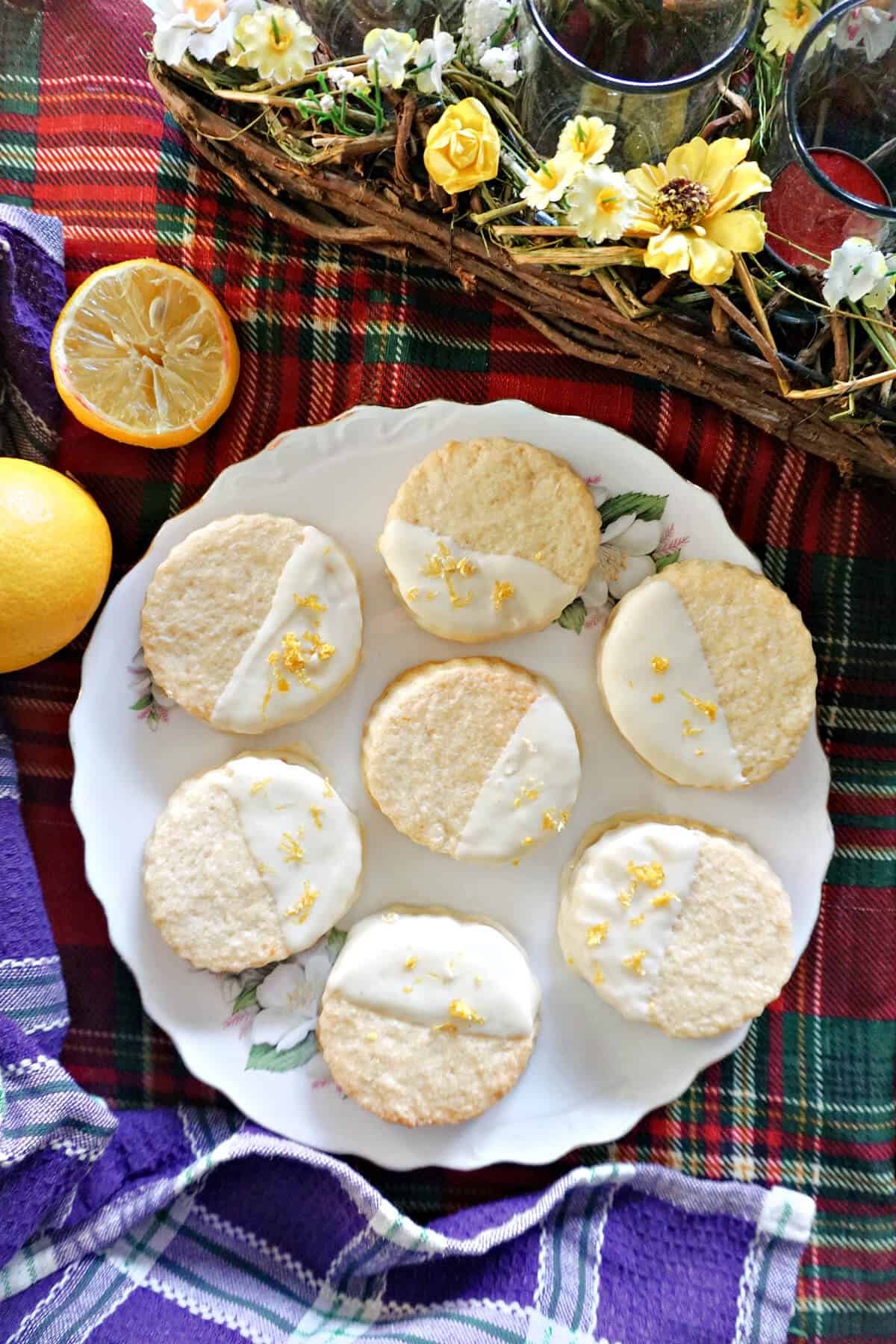A white plate with 7 cookies dipped in white chocolate and garnished with lemon zest and Easter decorations around.