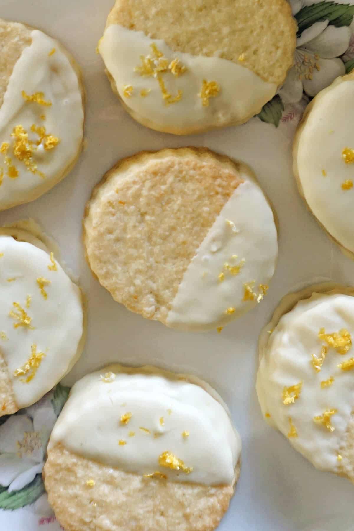 Close-up of a cookie covered partially in white chocolate and decorated with lemon zest, with other 6 partially-visible cookies around it.