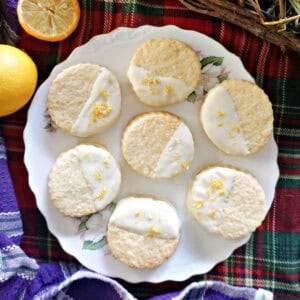 A white plate with 7 cookies dipped in white chocolate and decorated with lemon zest. Easter decorations around.