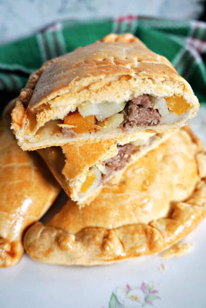 A white plate with a 2 whole pasties and 2 halves of a pasty to show how they look on the inside.