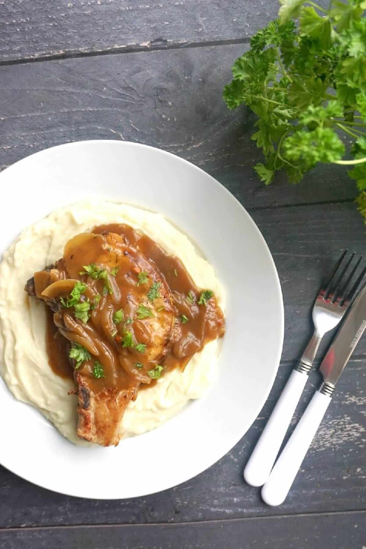 Overhead shoot of a white plate with a pork chop in gravy on a bed of mash.