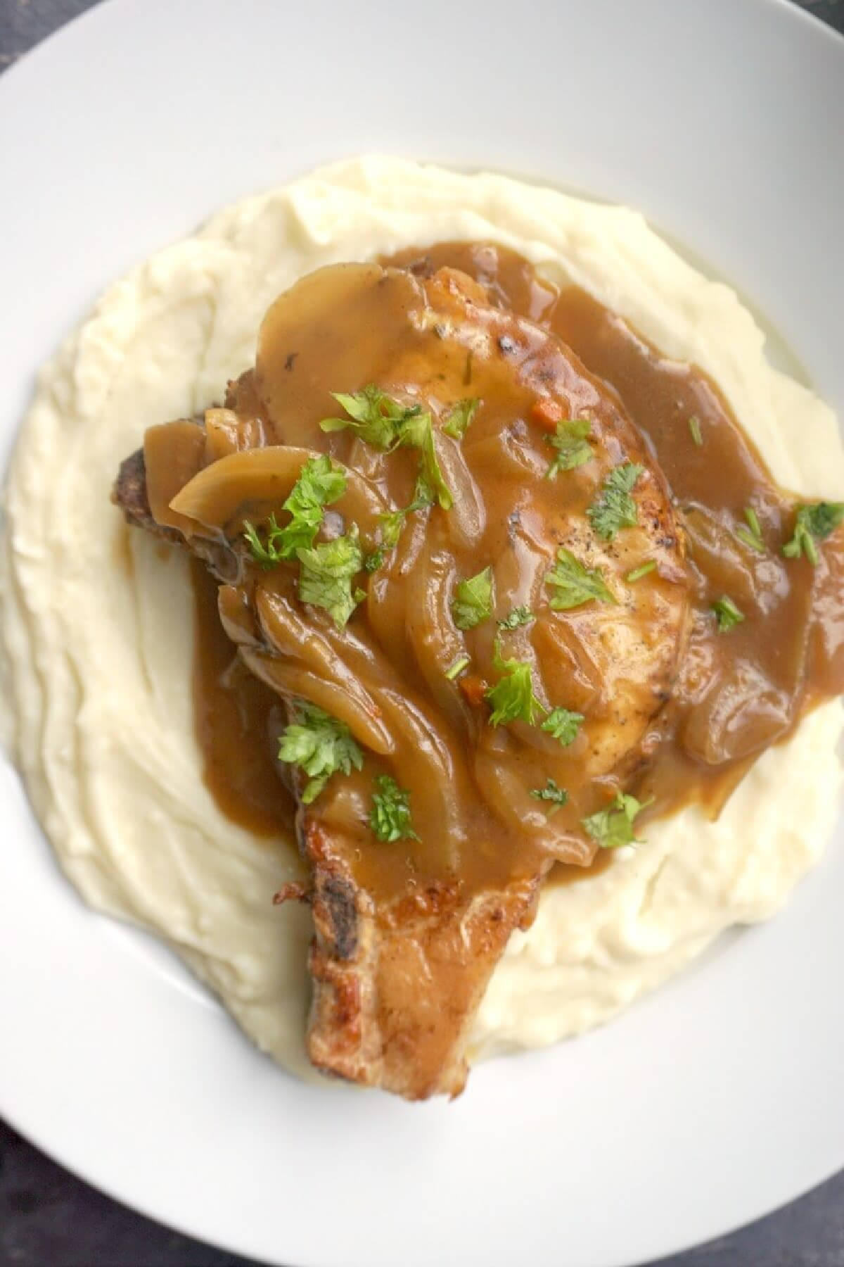 A white plate with a pork chops smothered in gravy on a bed of mash.