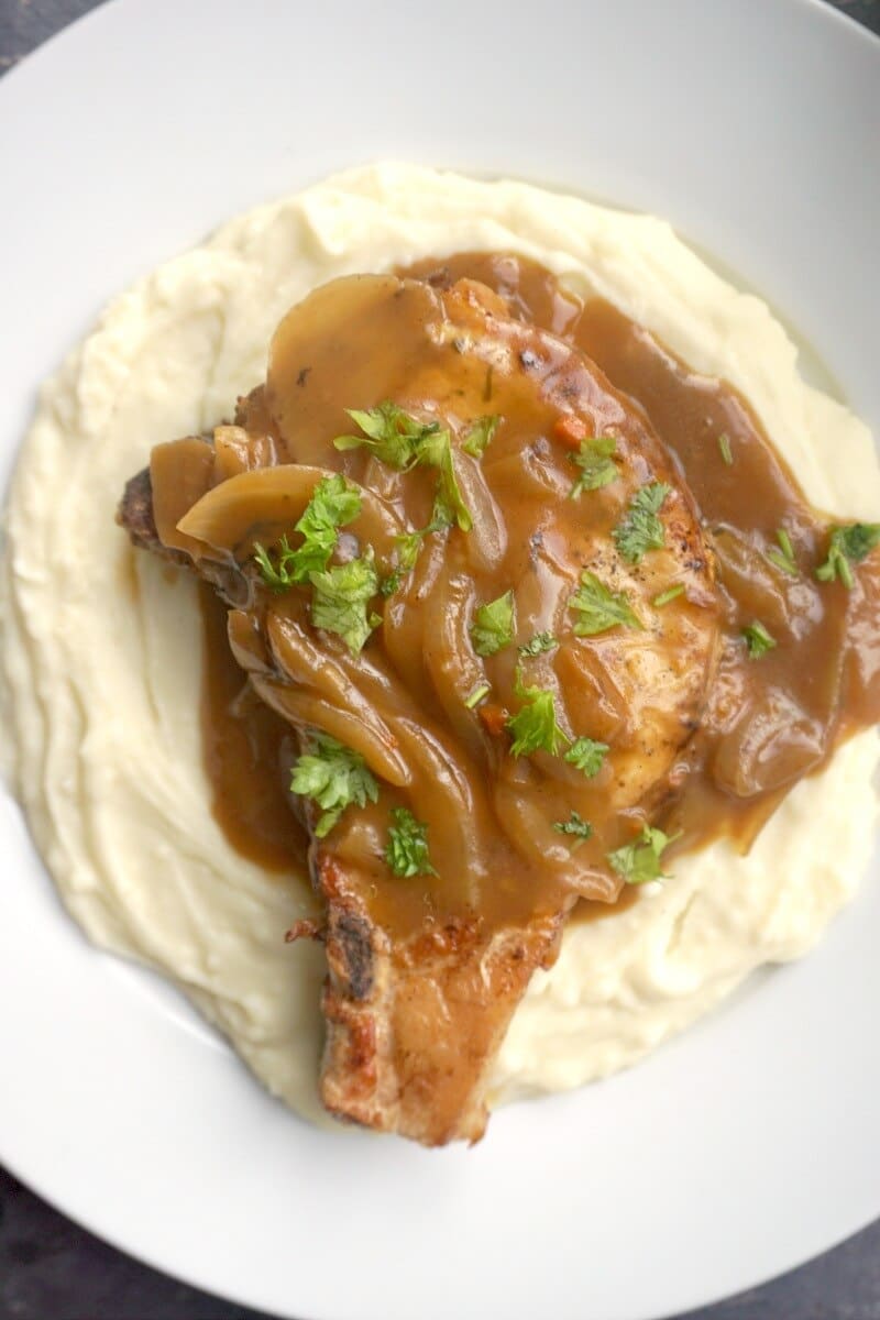 Overhead shoot of a white plate, mash and a pork chop smothered in onion gravy.