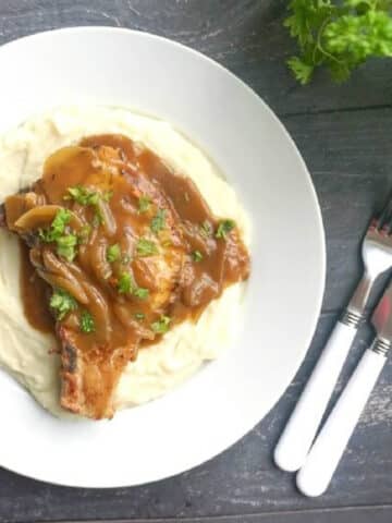 A white plate with a pork chop smothered in gravy on a bed of mash